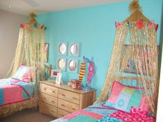 two beds in a room with blue walls and pink bedding, one has a canopy over it