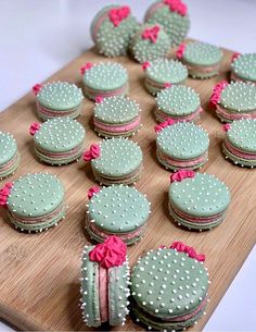 a wooden cutting board topped with cookies covered in green frosting and pink ribbon bows