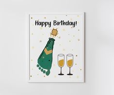 a happy birthday card with a bottle and two champagne glasses on the table next to it