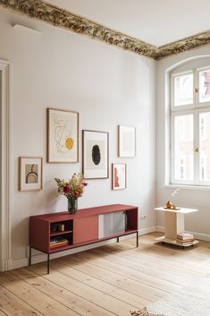 a living room with white walls and wooden flooring next to a red cabinet in front of a window