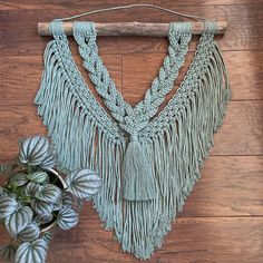 a green macrame hanging on a wooden wall next to a potted plant