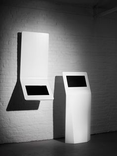 two white pedestals in front of a brick wall, one with a black screen on it