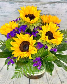 a bouquet of sunflowers and purple flowers in a vase on a wooden table