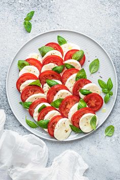 sliced tomatoes and mozzarella on a white plate with basil leaves around the edge