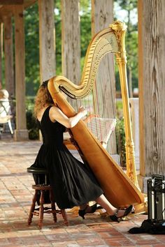 a woman in a black dress playing a large golden harp on a brick floored patio