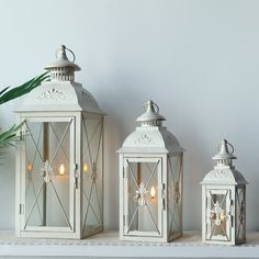 three white lanterns sitting on top of a shelf