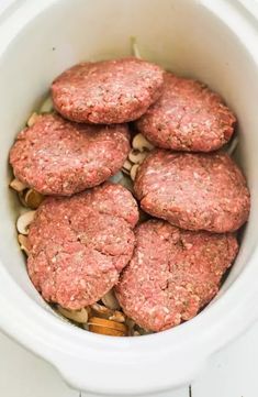 several hamburger patties in a white crockpot with nuts on the side, ready to be eaten