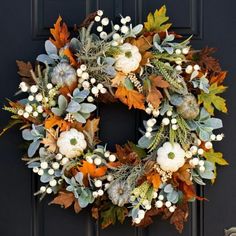 a wreath with white pumpkins and greenery hangs on the front door's black door