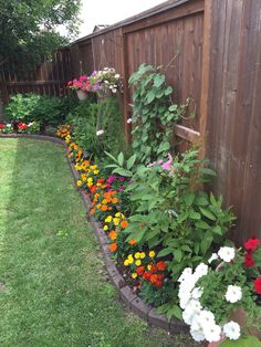 a garden filled with lots of colorful flowers next to a wooden fence and green grass