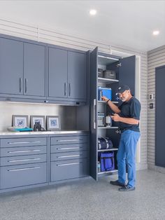 a man standing in front of a blue cabinet with drawers and cabinets behind him, holding a clipboard that is attached to the wall