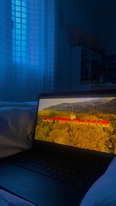 an open laptop computer sitting on top of a bed in a room with blue curtains