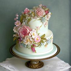 a three tiered cake decorated with pink flowers on a white tablecloth and gold trim