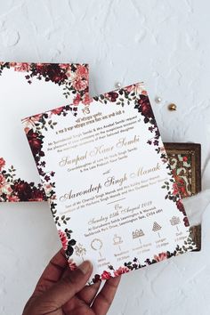 a person holding up two wedding cards in their hand, with flowers on the front and back