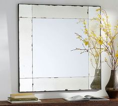 a mirror sitting on top of a wooden shelf next to a vase with yellow flowers