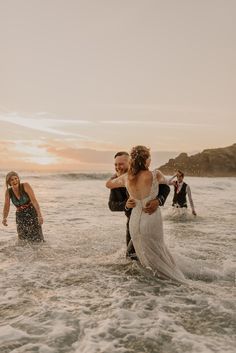 a bride and groom walking into the ocean at sunset with their arms around each other