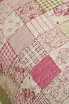 a pink and white quilt on top of a bed next to a pillow with flowers