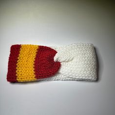 a crocheted hat with a red and yellow stripe on the front, sitting on a white surface