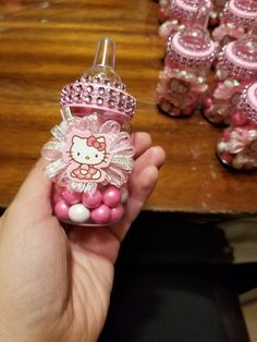 a hand holding a hello kitty bottle with pink candy in it and lots of other bottles behind it