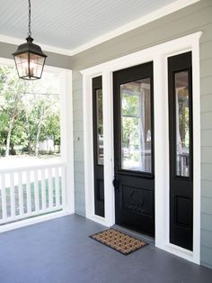 the front door of a house with two black double doors and a brown mat on the floor