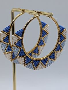 two pairs of blue and white beaded hoop earrings on a gold plated stand