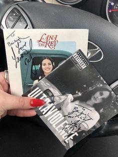 a person holding up an autographed book in their hand next to a car steering wheel