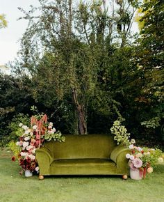 a green couch sitting in the middle of a lush green field next to a tree