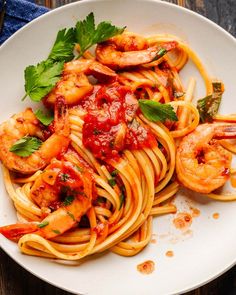 pasta with shrimp, tomato sauce and parsley on a white plate sitting on a wooden table