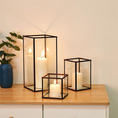 three lit candles sitting on top of a wooden table next to a potted plant