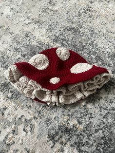 a red and white crocheted hat laying on top of a rock covered in dirt