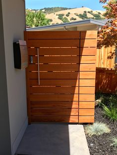 a wooden door in the side of a house next to a tree and fence with mountains in the background