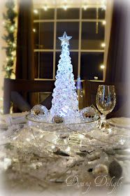 a glass christmas tree sitting on top of a table next to two wineglasses