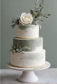 a three tiered cake with white flowers and greenery on top, sitting on a pedestal