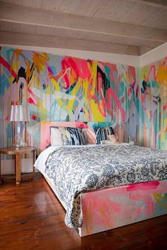 a large bed sitting in a bedroom next to a wall covered in colorful graffiti paint