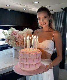 a woman holding a pink cake with lit candles