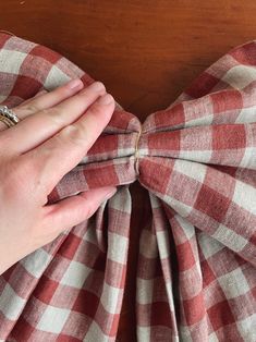 a person tying a bow tie on top of a red and white checkered shirt