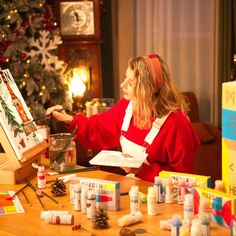 a woman in red shirt painting on easel next to christmas tree and other decorations