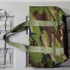 a green and brown camouflage bag hanging on the wall next to a metal rack with hooks