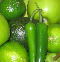 a pile of green apples and cucumbers with peppers on the top one has an eggplant in it