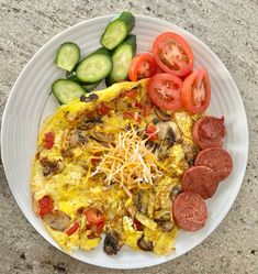 a white plate topped with an omelet covered in cheese and toppings next to sliced cucumbers