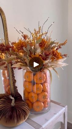 a vase filled with lots of oranges on top of a white table next to a mirror