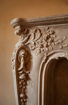 an ornate white fireplace with flowers and vines on the mantle, against a beige wall