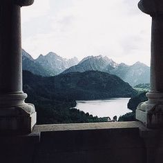 an open window with mountains in the background and water on the other side that is surrounded by columns