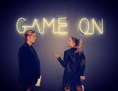 two women standing next to each other in front of a neon sign that says game on