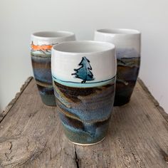 three cups sitting on top of a wooden table next to each other with trees painted on them