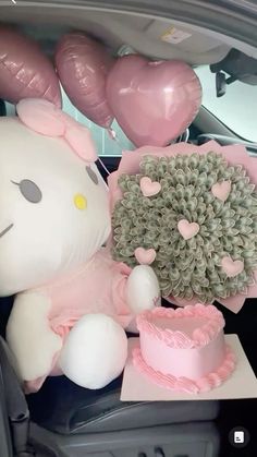 a hello kitty stuffed animal sitting in the back seat of a car next to a cake and balloons