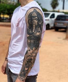 a man with a tattoo on his arm standing in front of some cars and holding a skateboard