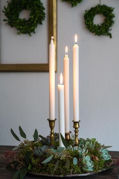 four candles are lit on a table with greenery