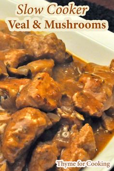 a white plate topped with meat and mushrooms covered in gravy on top of a table