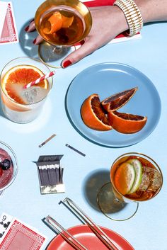 two people are holding their glasses with oranges and other drinks on the table next to them