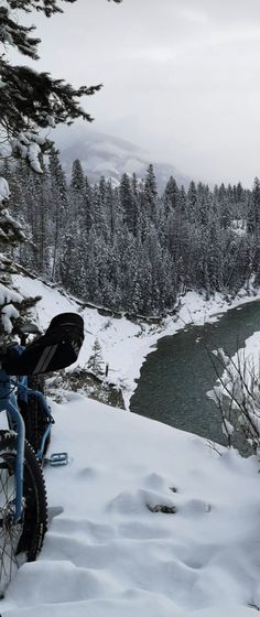 a bike parked on the side of a snow covered hill next to a lake and forest